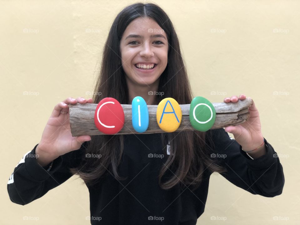 Adolescent girl holding a multi colored stones composition of the italian word Ciao