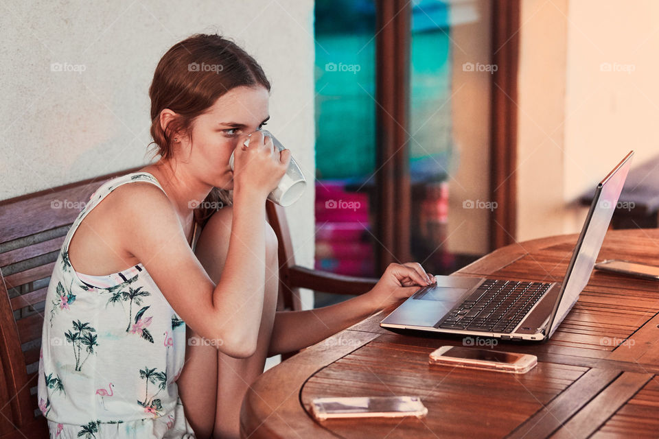 Woman working at home, using portable computer, sitting on patio on summer day. Candid people, real moments, authentic situations