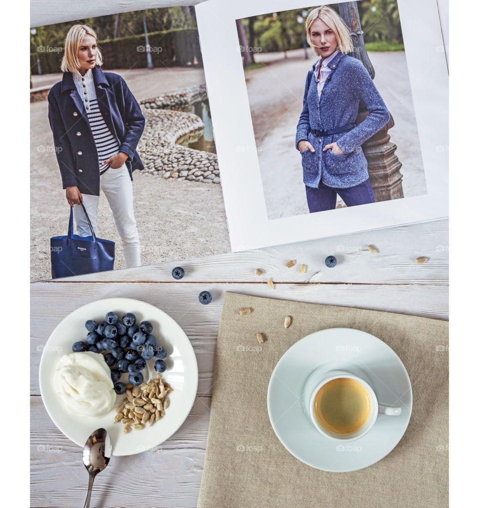 Morning coffee with a fashion magazine.  Food photo, square orientation, flat lay.  Girl's breakfast: a cup of espresso with a catalog of branded clothes, with blueberries, seeds and yogurt.  Useful nice breakfast