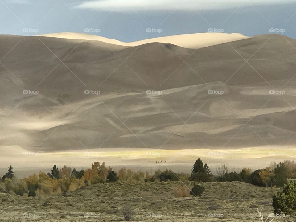 Great Sand Dunes with shadows and three people hiking very tiny