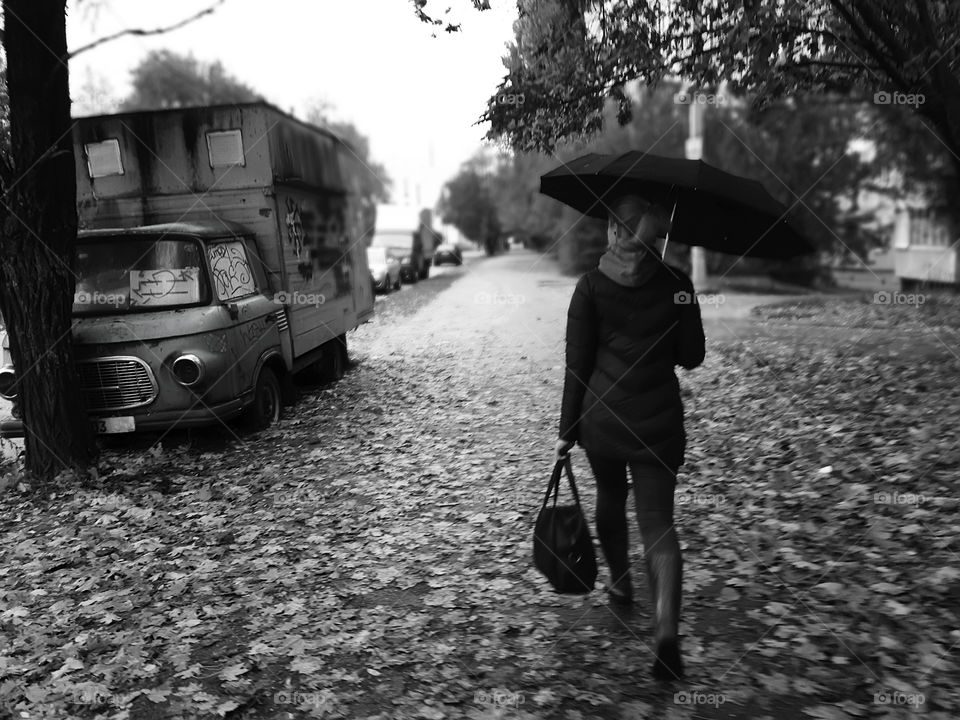Young woman rushing under the autumn rain through the city park with fallen leaves 
