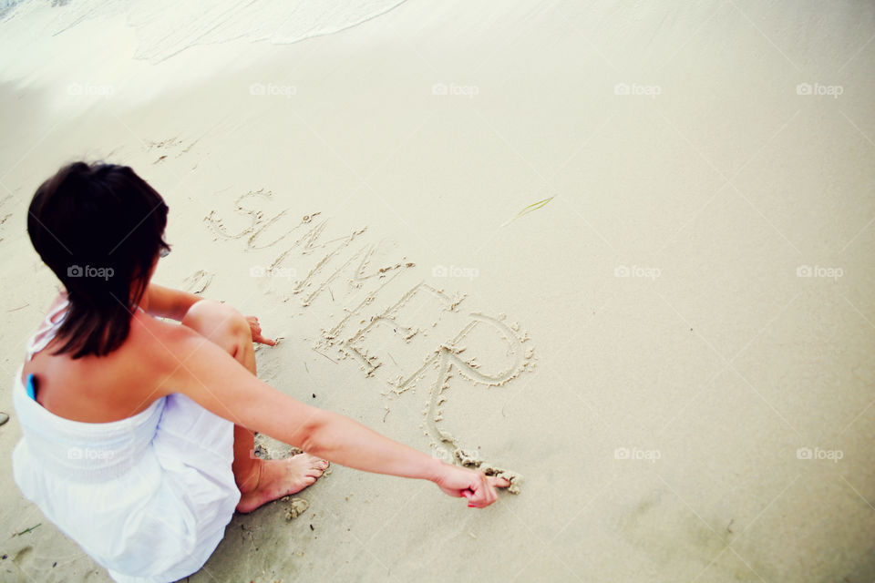 Woman writing summer on sand 