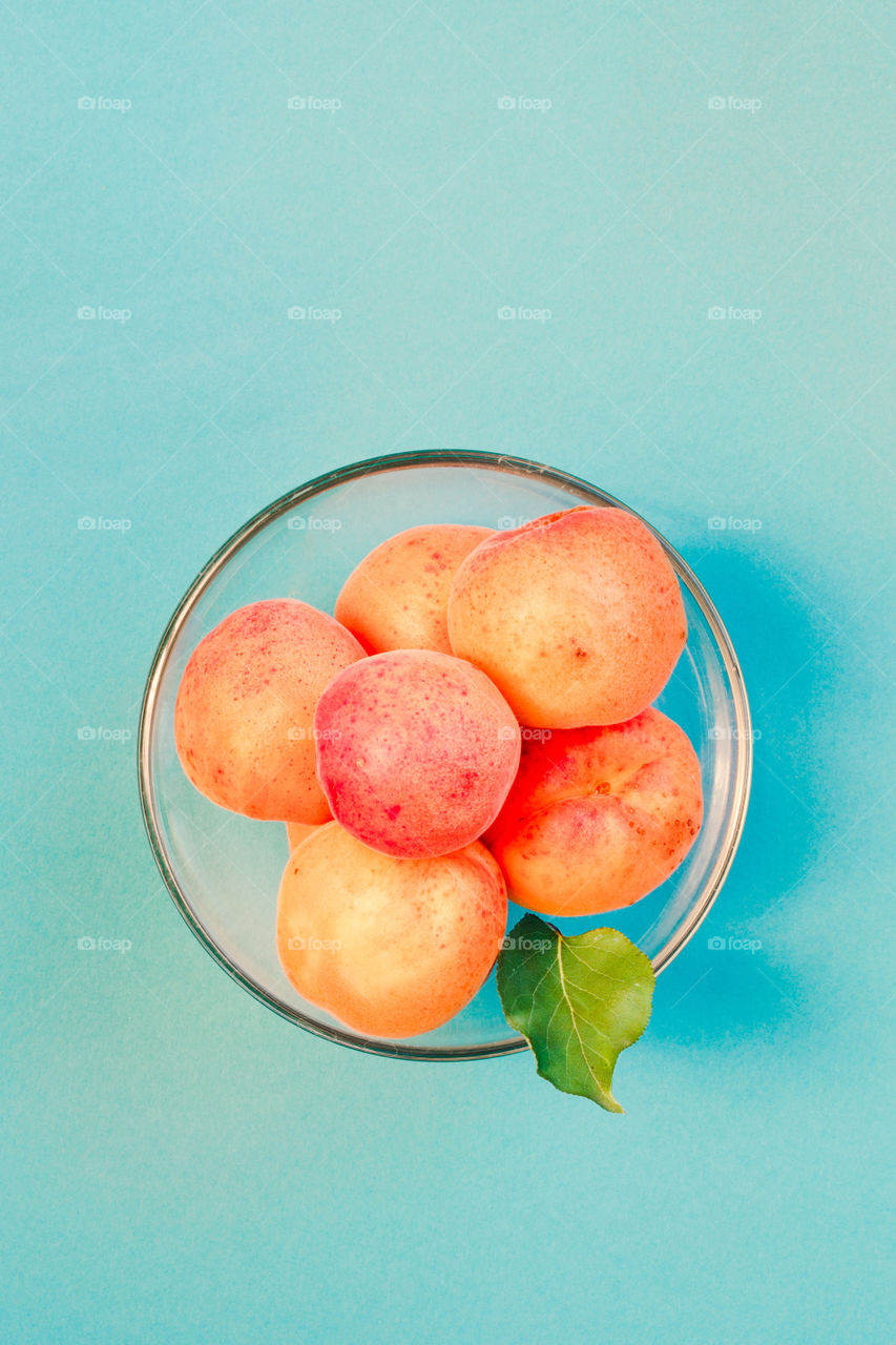 Fresh apricots picked straight from tree in the garden in bowl on plain blue background