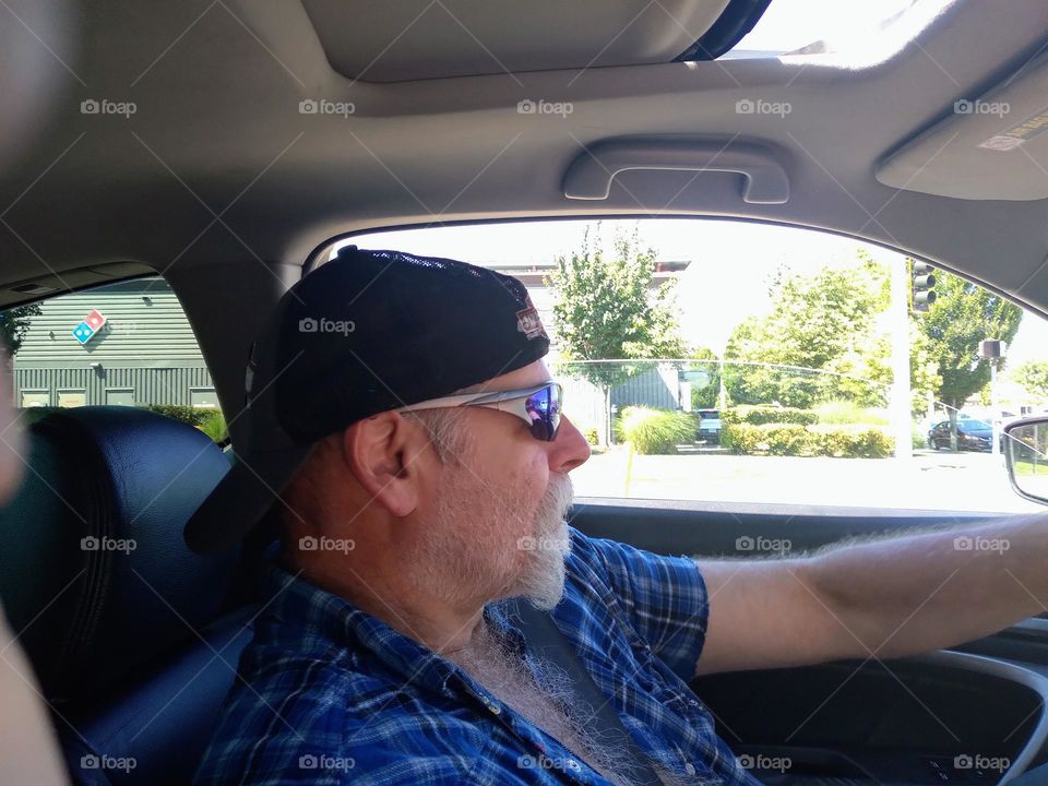 Bright sunny day, man with dark shades and a backwards baseball cap in his vehicle on the way to work to his construction company.