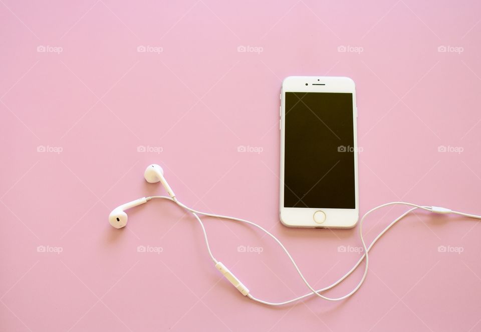 Cell phone and ear buds on a pink background flat lay 