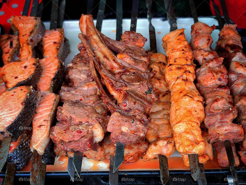 Food. There are metal skewers on the grill. Each skewer has different types of meat and fish: salmon steaks, trout steaks, lamb loin, pork cuts, beef cuts and chicken cuts