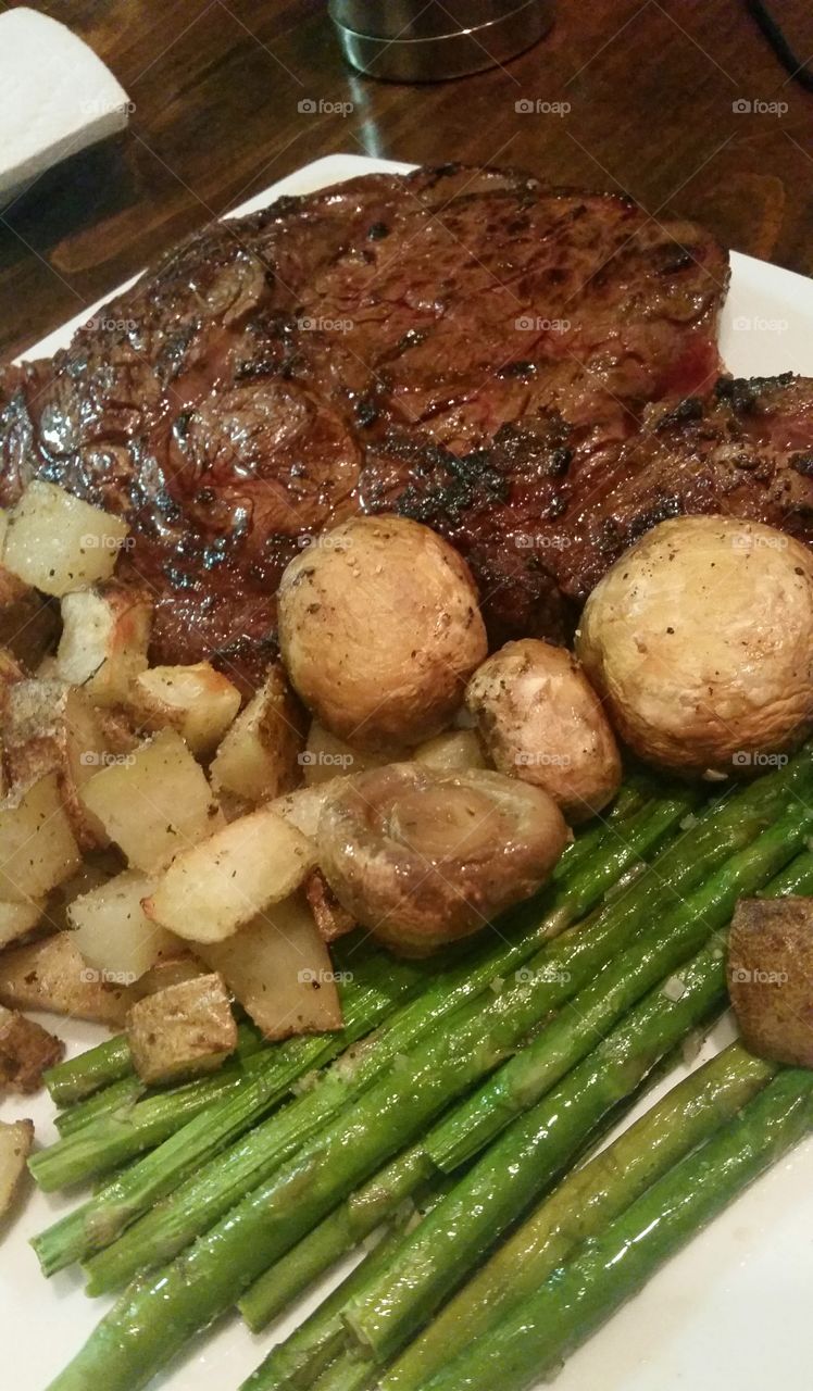 a nice juicy ribeye steak with roasted potatoes and green asparagus