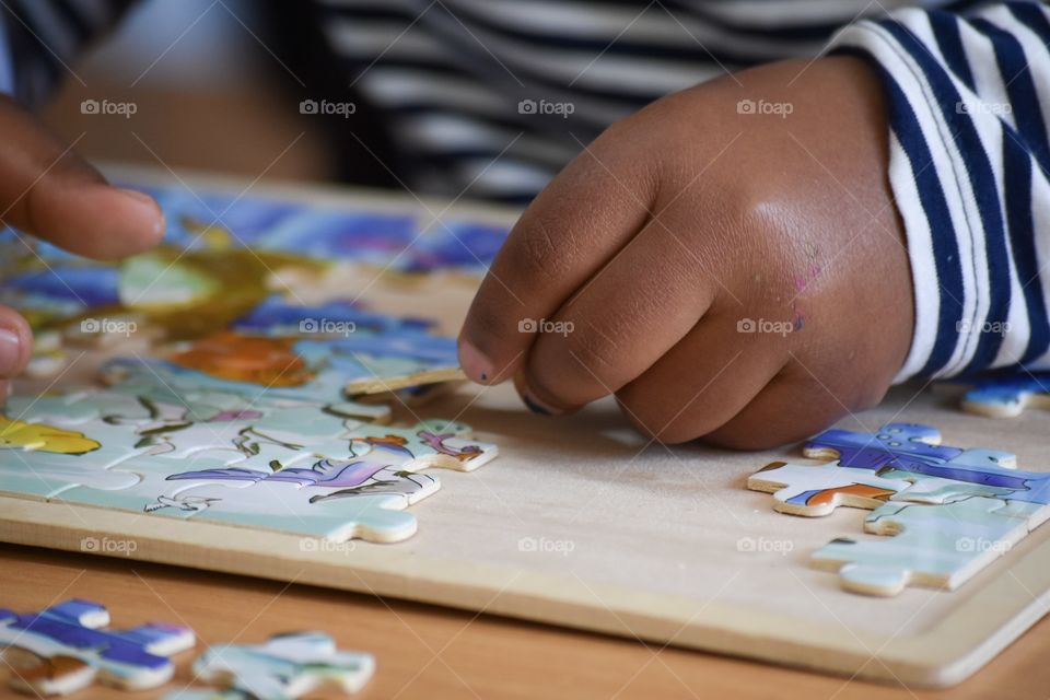 Preschool 4 year old african American child building a puzzle with his small, delicate hands