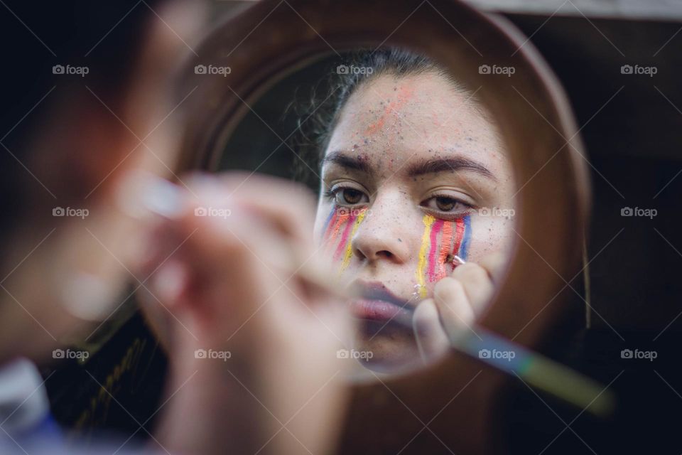 Photograph of sad girl painting her face with colorful paint