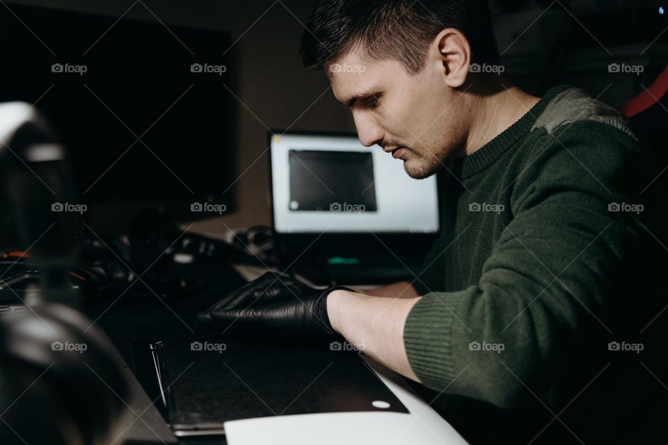 Portrait of a young handsome Caucasian male brunet working at his desk and repairing his laptop at night by the light of a lamp, close-up view from the side.