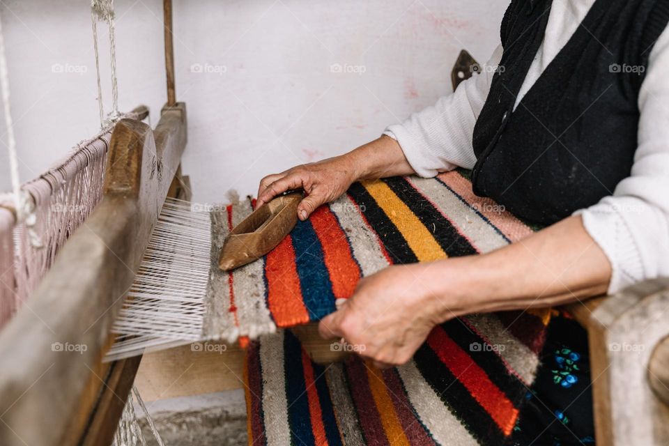 Woman making a carpet from wool material, at a very old loom machine, in a rural village from Romania.