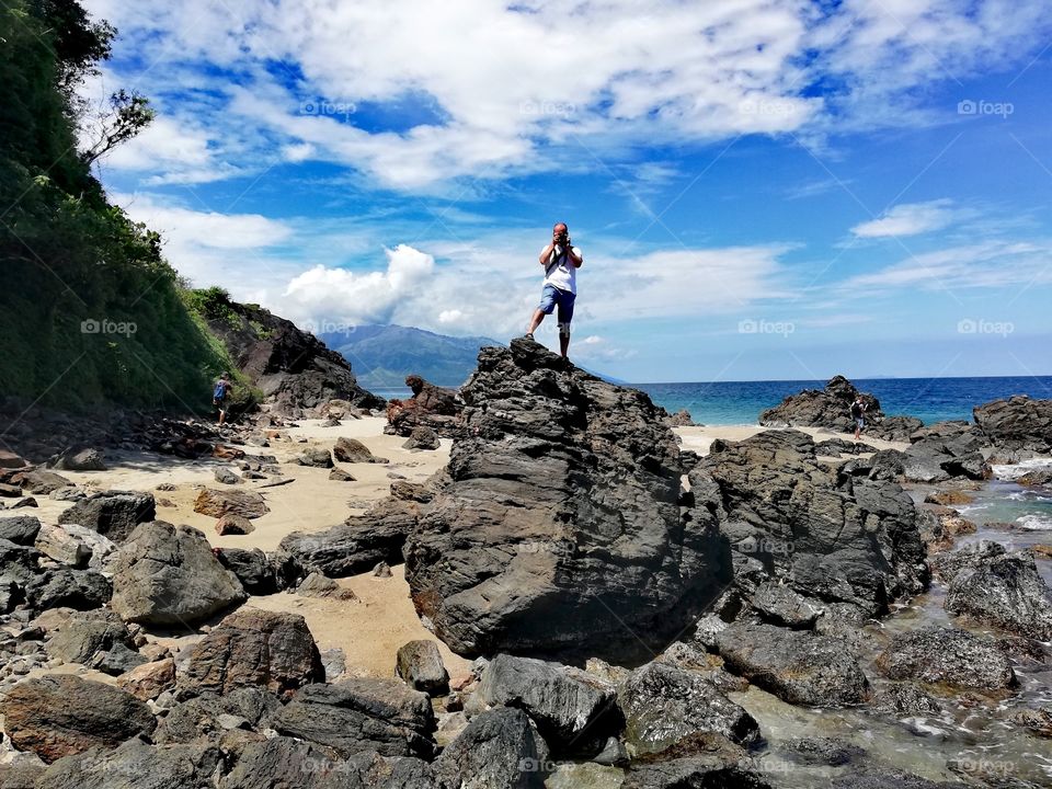 Man standing on a basaltic volcanic rock on the beach, taking pictures of beach, in Mindoro, Island of Philippines