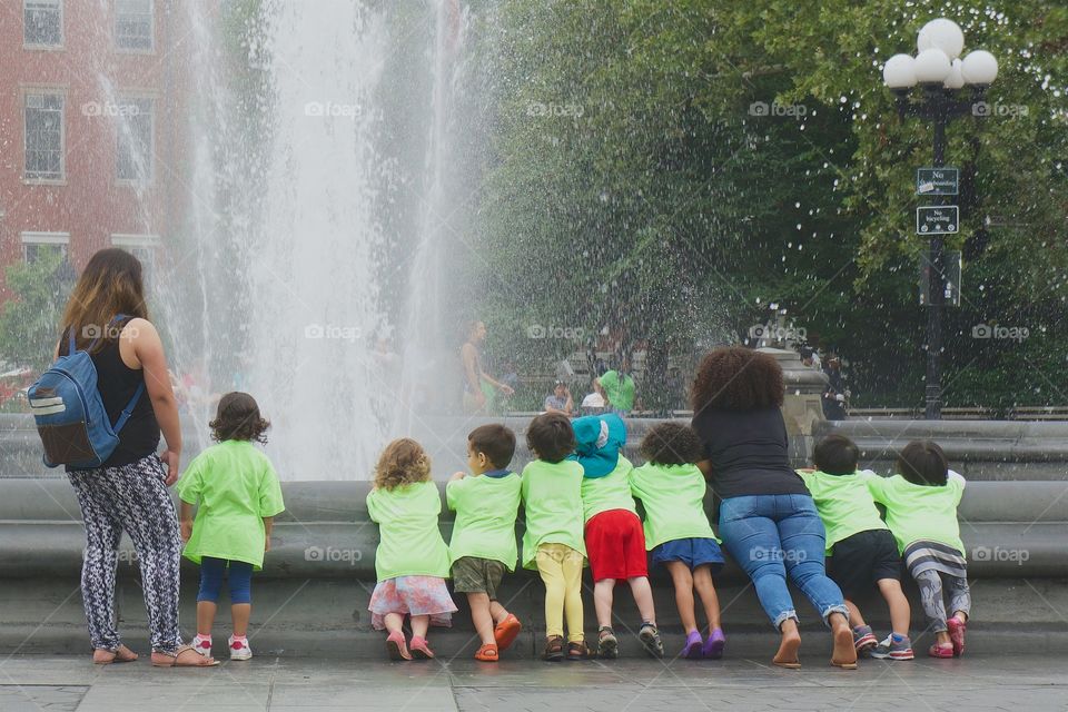 A group of children with adult supervision enjoying the view of the water fountain in Washington Square Park, Manhattan, New York City.