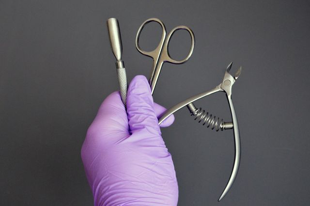 Manicure tools are held by a manicurist in rubber gloves