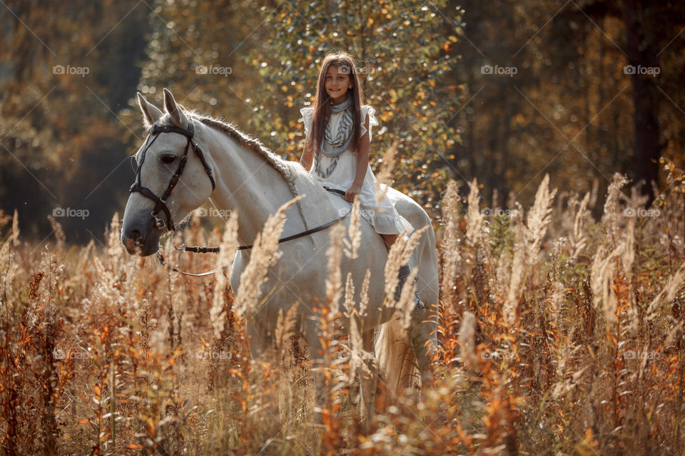 Little girl with grey horse in autumn park 