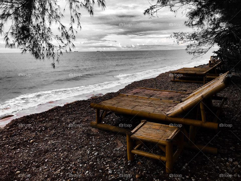 Bamboo beach chairs by pebble seashore before the storm in monotone black and white color 