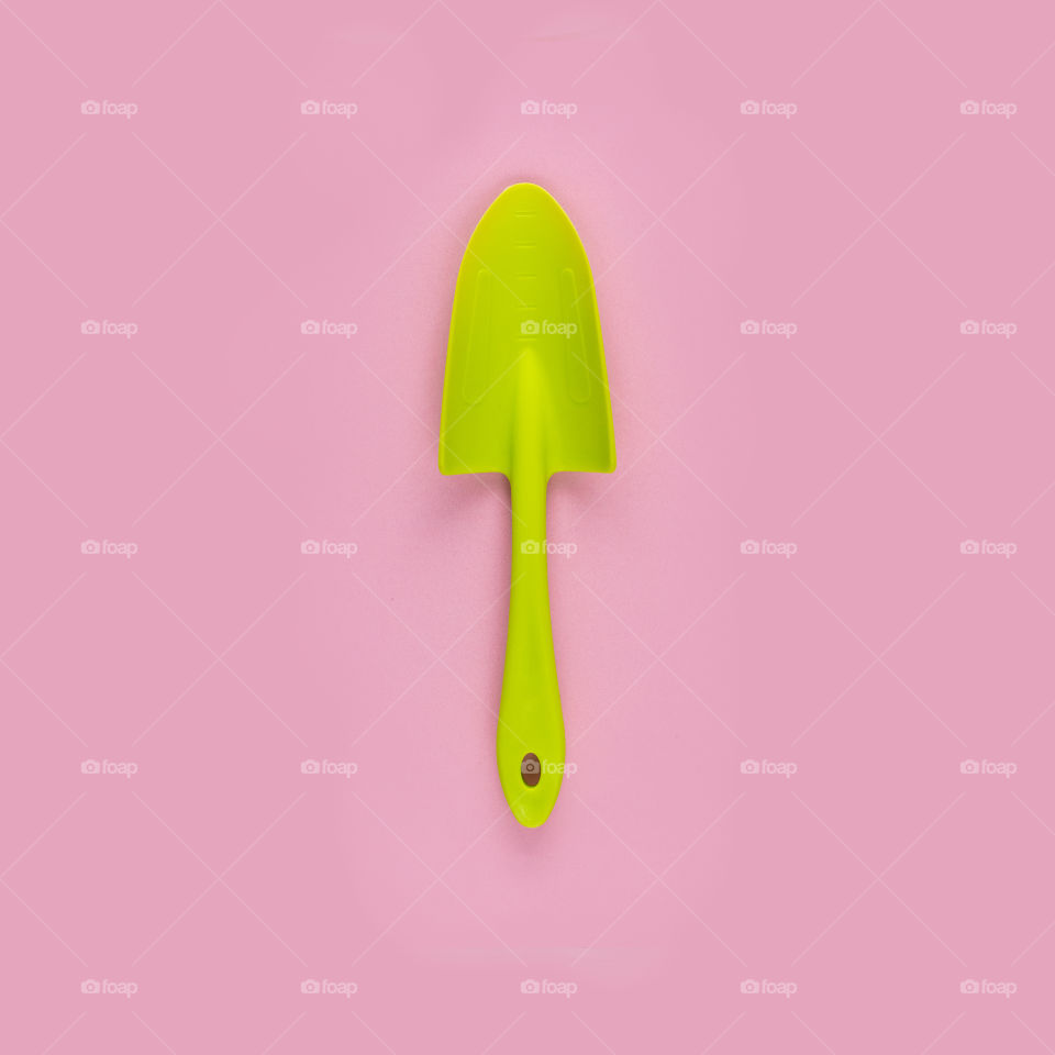 Green shovel on pink background. Minimalistic photography. Contrast colors