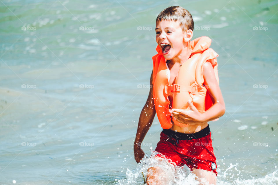 Happy laughing boy in orange inflatable vest swimming in the sea 