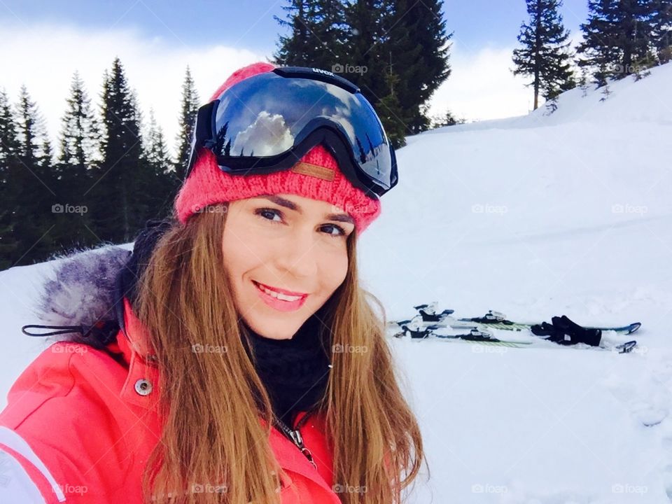 Selfie of woman with ski glasses on and skis in the background 