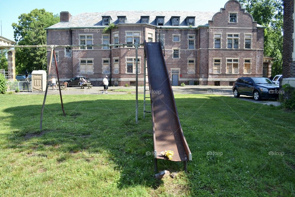 An old rusted metal slide on the grass in front of an old abandoned brick building