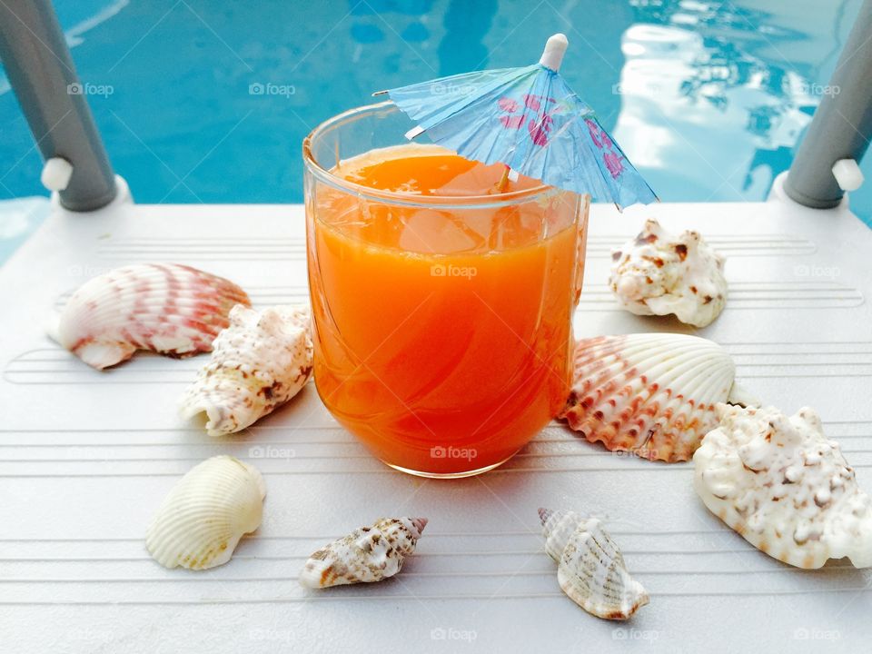 Orange juice with blue umbrella and seashells