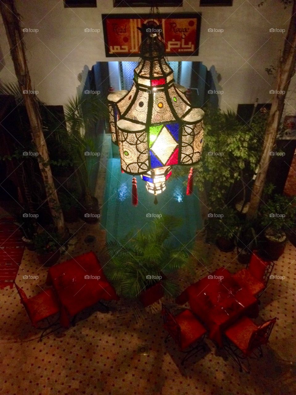 A decorative stained glass chandelier over a small pool and colorful tables in a riad in Marrakech, Morocco 