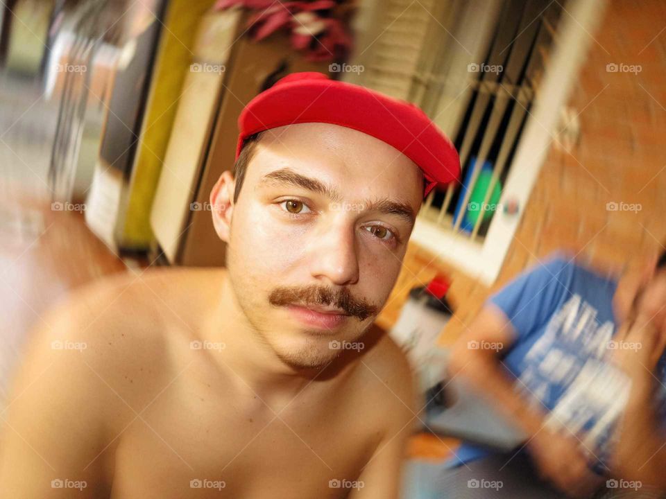 Portrait focus on man, swirly bokeh achieved by rotating the camera. Man with mustache and a red hat.
