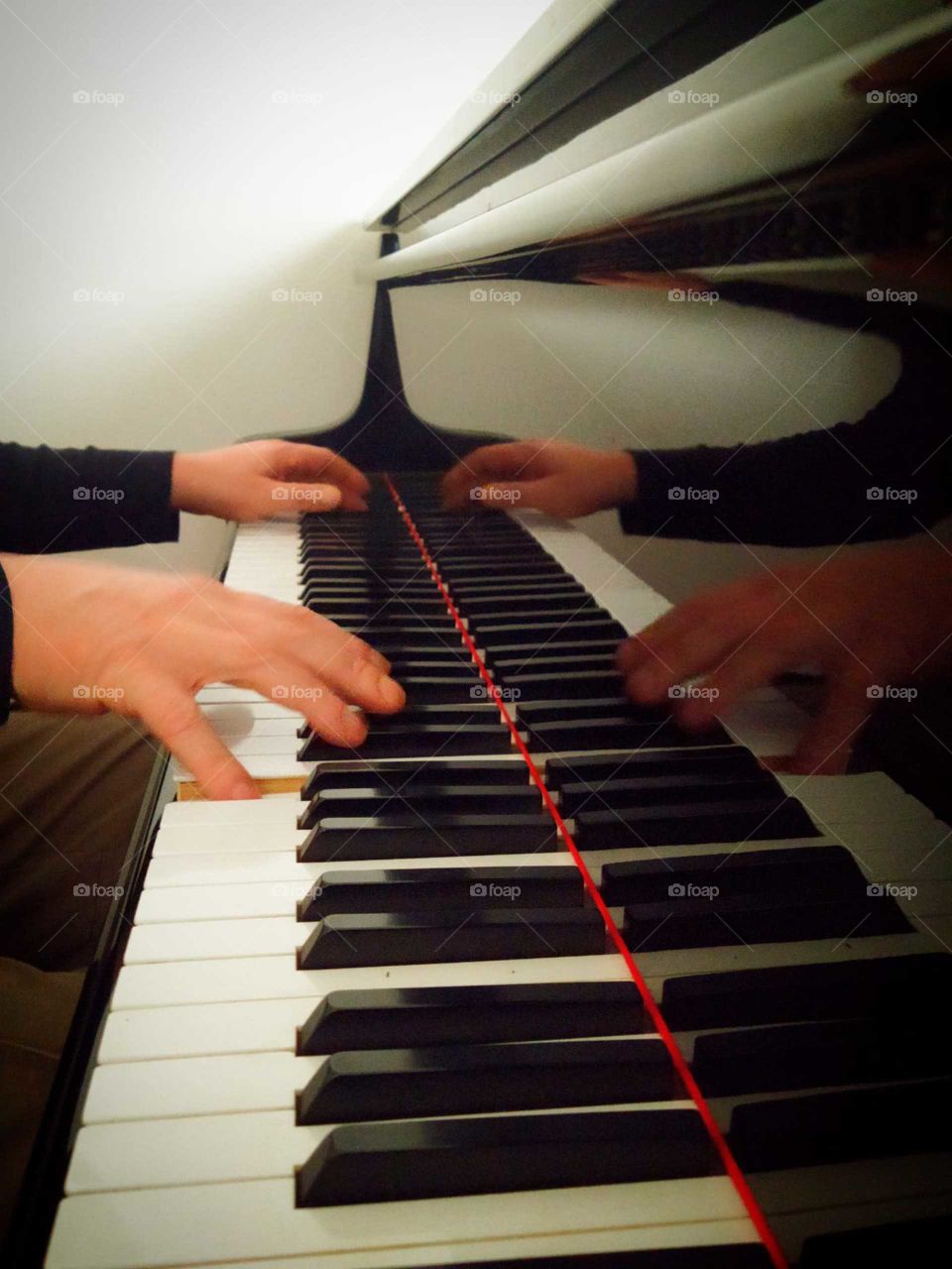 Reflection.  Male hands on the keys of the piano.  Reflection of hands from a black polished piano lid