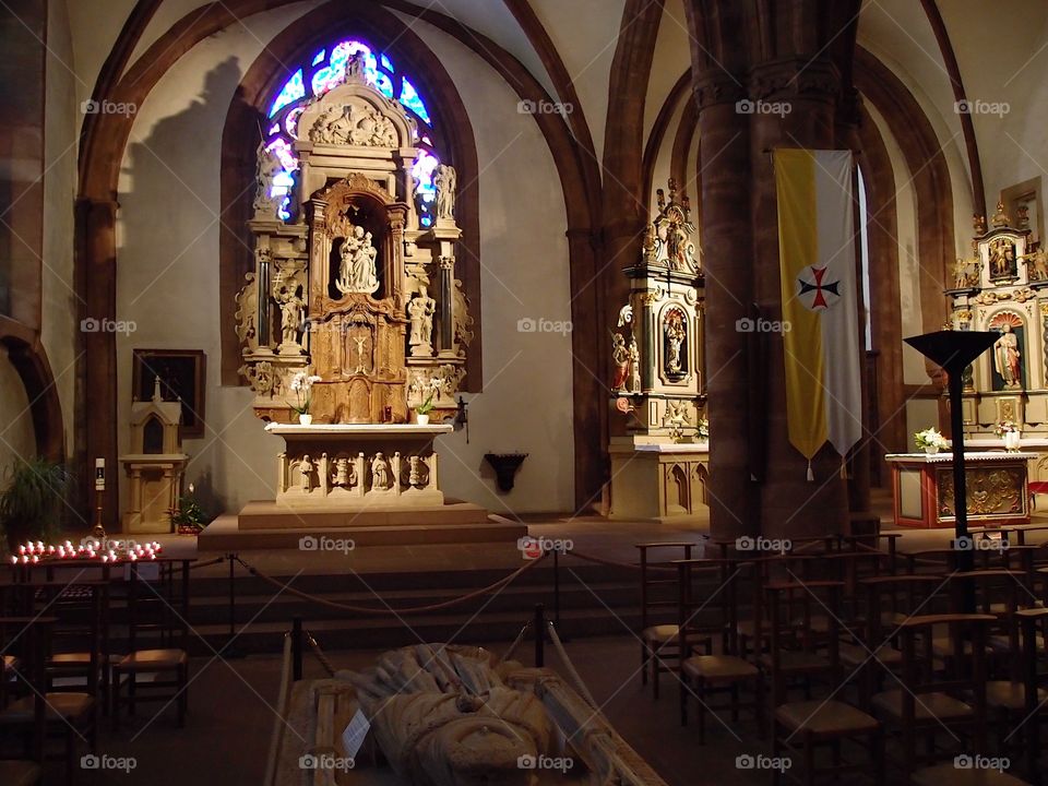 The beautiful interior of an old Cathedral with a tomb and highly decorated alter with a stained glass window in the background in Luxembourg.