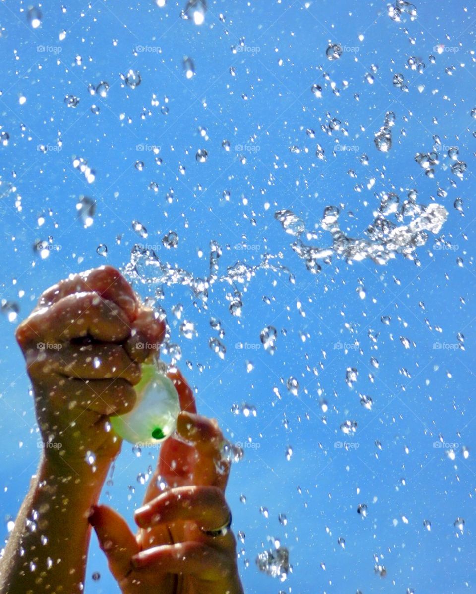 Person popping a water balloon in their hands with water going everything 