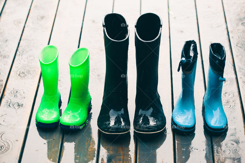 Row of wellies in various sizes standing on a wooden porch while raining