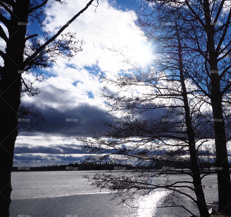 Spring weather in Finland. Sunshine and blue sky. Icy lake is finally begun to melt. Tree and clouds brings nice contrast to this picture.