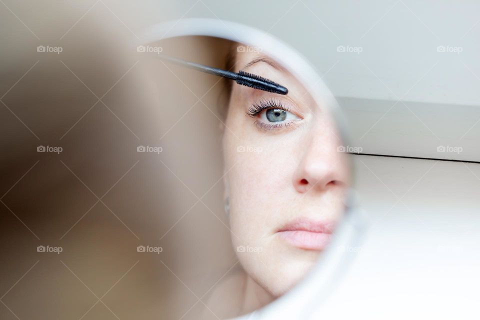 Woman applying mascara to her eyes, reflection in the mirror