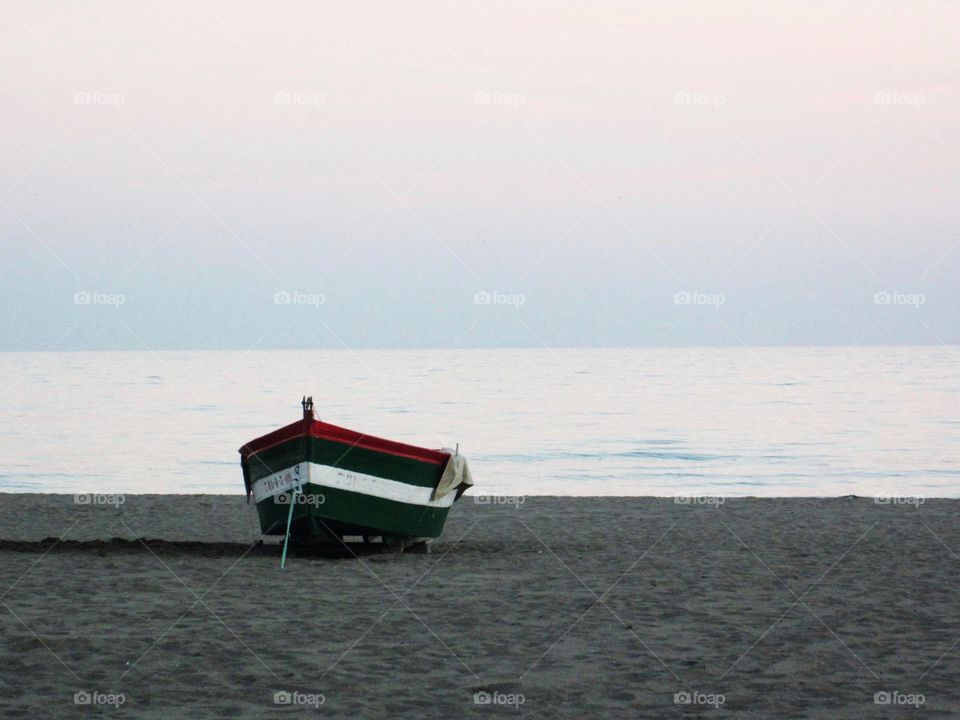 Boat on the sand near the sea . Lonely boat on sand by the sea. The sea calm. Sky at sunset has a pink shade. 