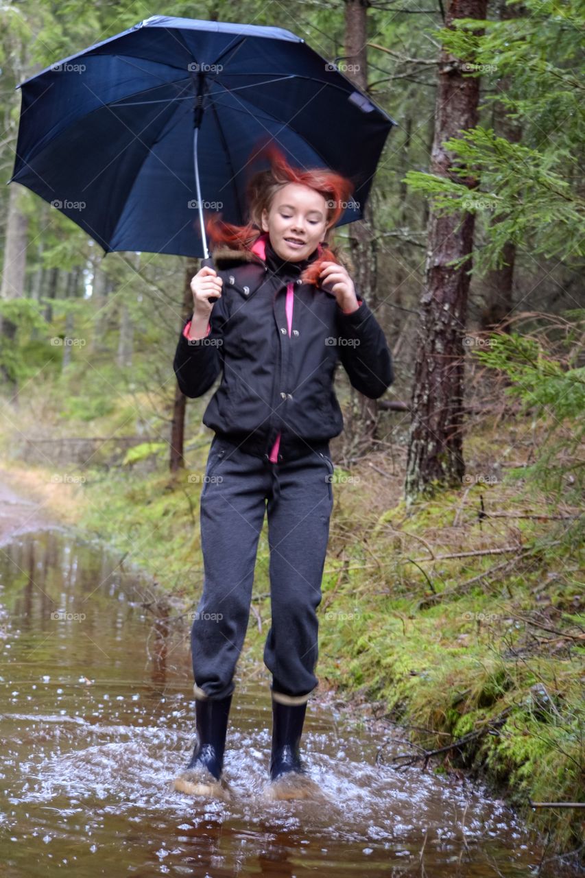 Girl jumping in a puddle with an umbrella a rainy day