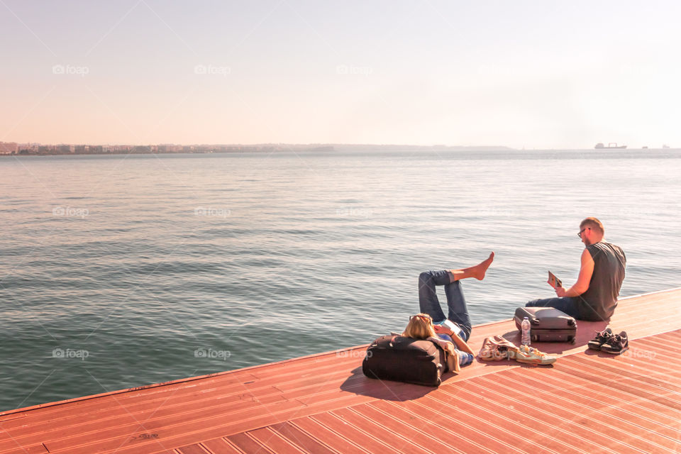 Young Couple Resting And Reading Books At The Dock In Front Of The Sea
