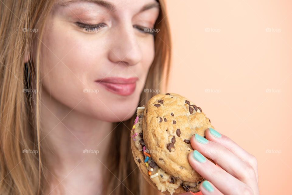 Closeup of a woman smiling and holding a chocolate chip cookie sandwich 