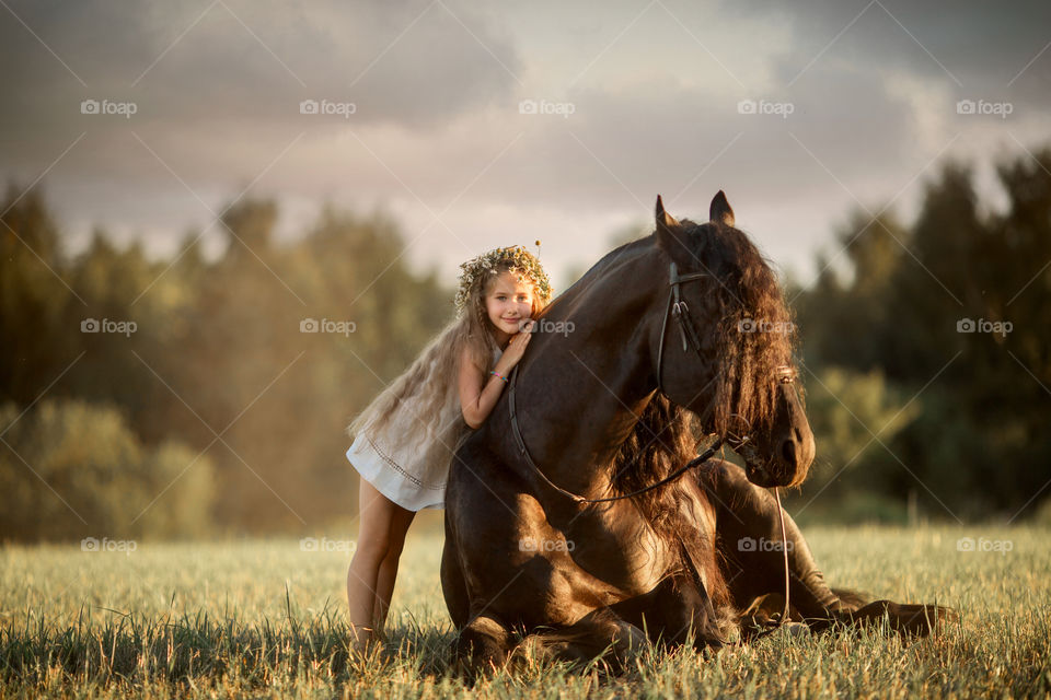 Little girl with black fresian stallion at summer evening