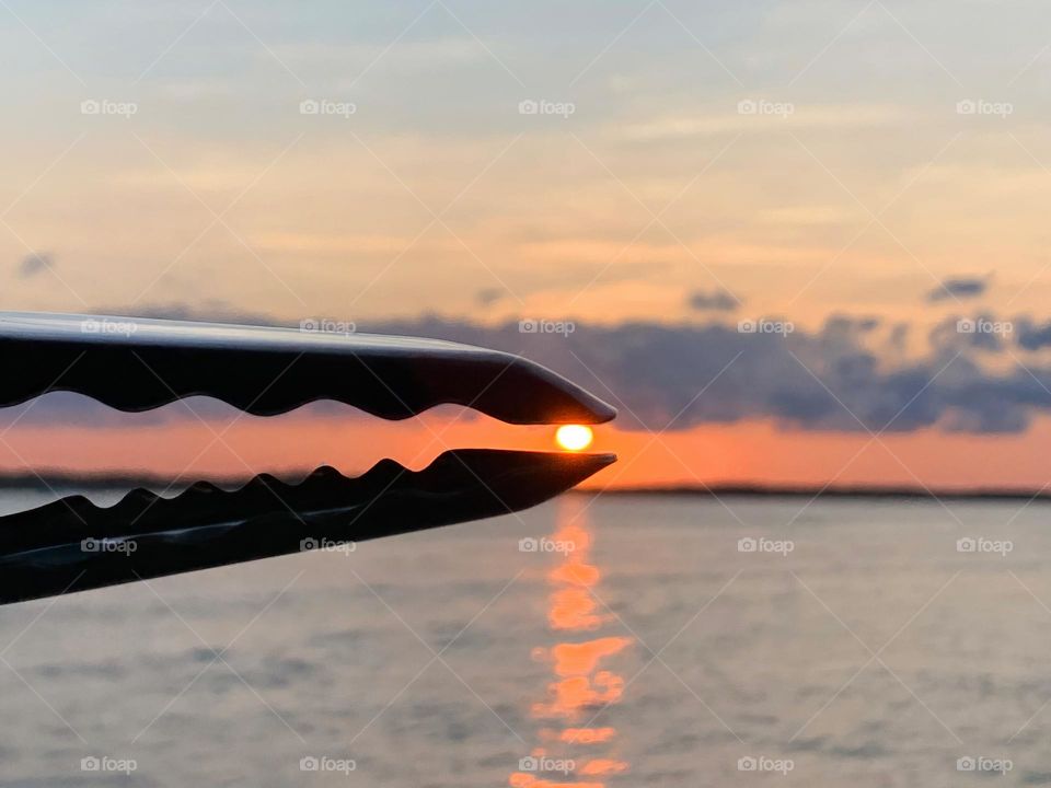 Sunset held by a barbecue metal tongue effect or illusion for a start of a summer rest and comforting to watch in the horizon with reflection on the Indian lagoon river. 