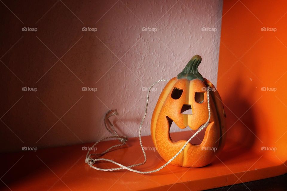 An orange Halloween decoration pumpkin stands on an orange shelf in front of a white wall