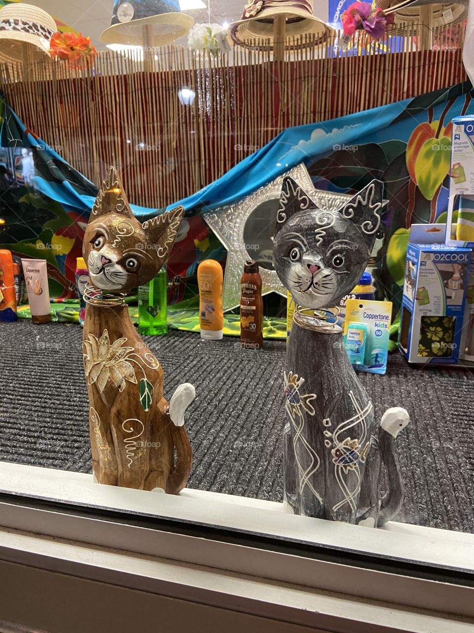 Wood carved kitties in a shop window, looking at passersby. 