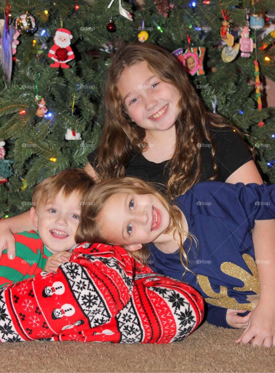 Brother and sisters sitting against christmas tree decoration