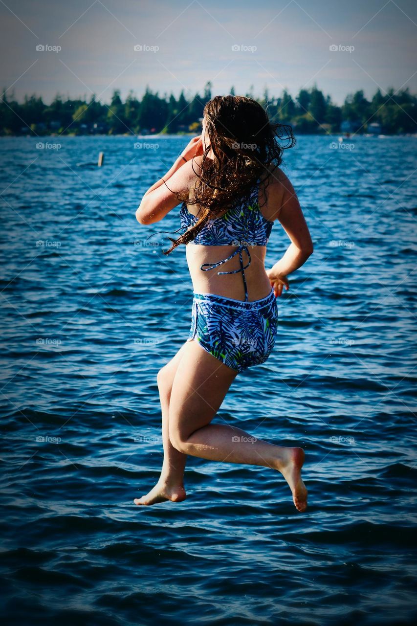 A young woman readies herself as she jumps into a vibrant blue lake on a sunny summer day 