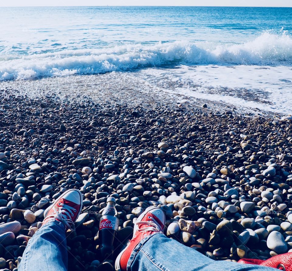 A bottle of Diet Coke on the beach in Nice with red sneakers.