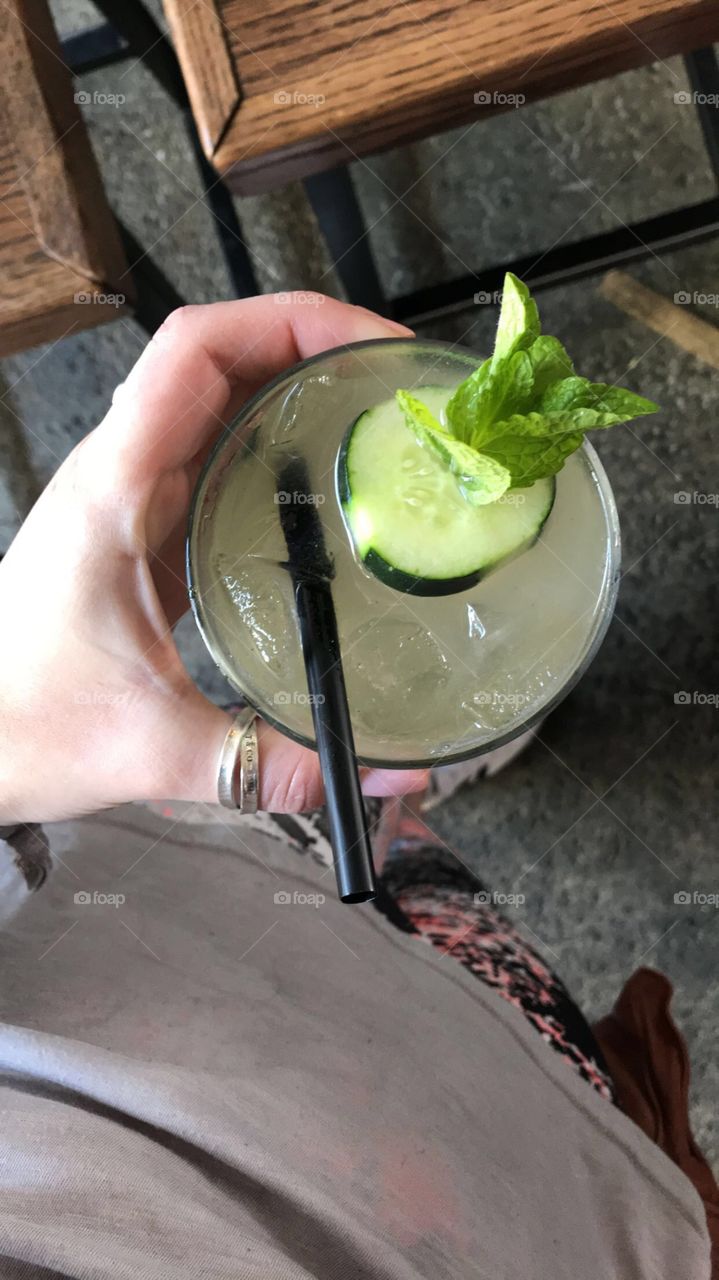 Holding a cucumber cocktail with ice and straw and mint