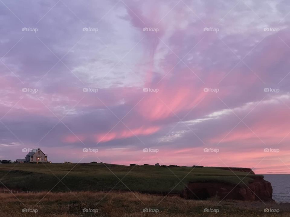 Pinked clouds after sunset in the sky with a house of the top of the hill. Îles-de-la-Madeleine, Québec, Canada.