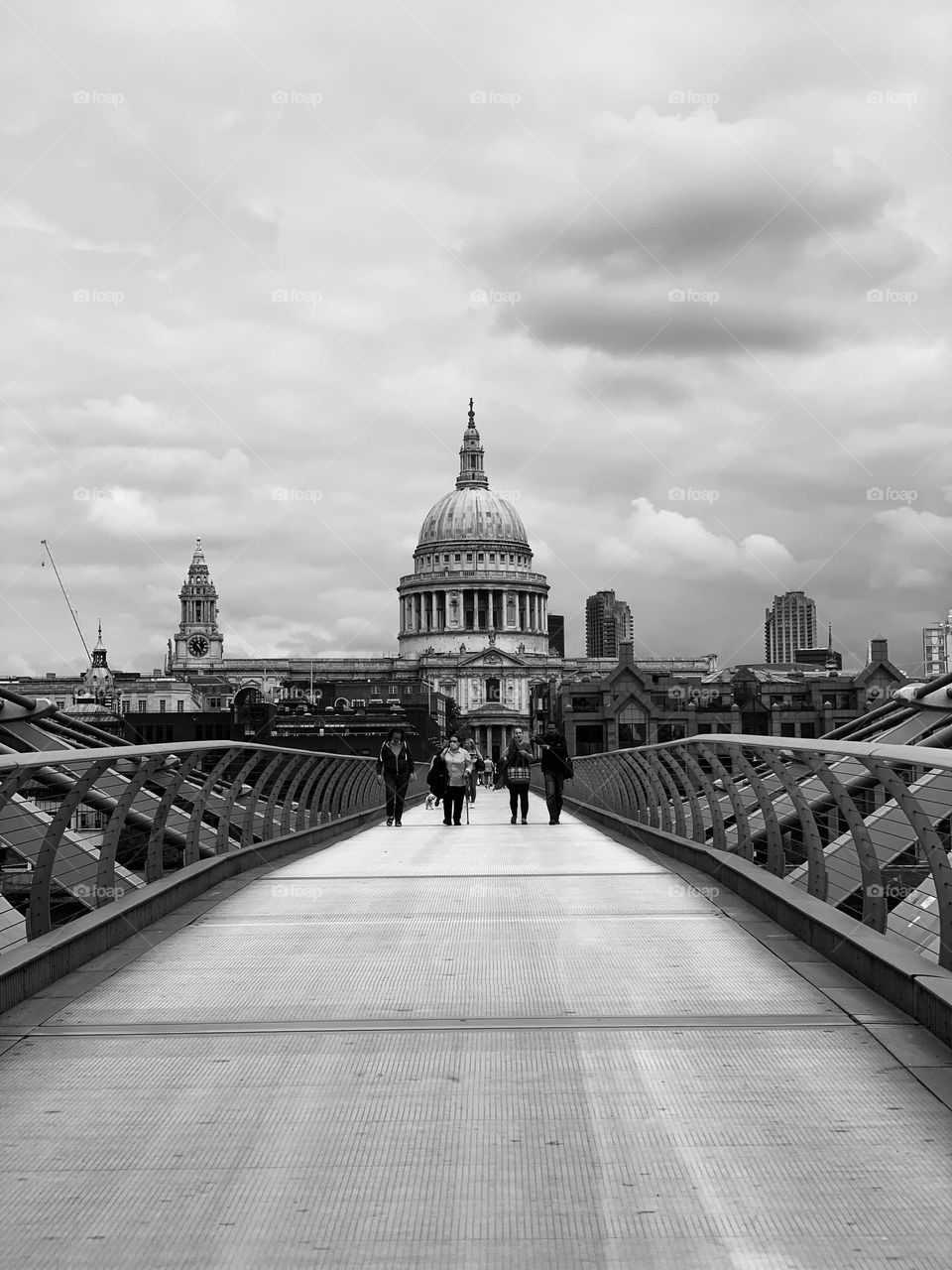 View of St Paul’s cathedral from south bank side of Millennium Bridge in London, UK, black and white, cloudy sky, unrecognizable people 