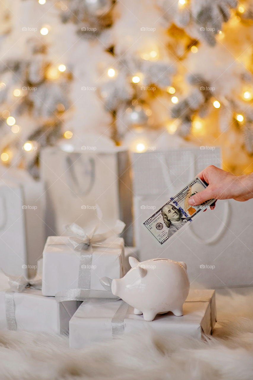 piggy bank with 100 dollars banknote in festive New Year atmosphere of scenery.  Magical bokeh with Christmas tree and bright lights.