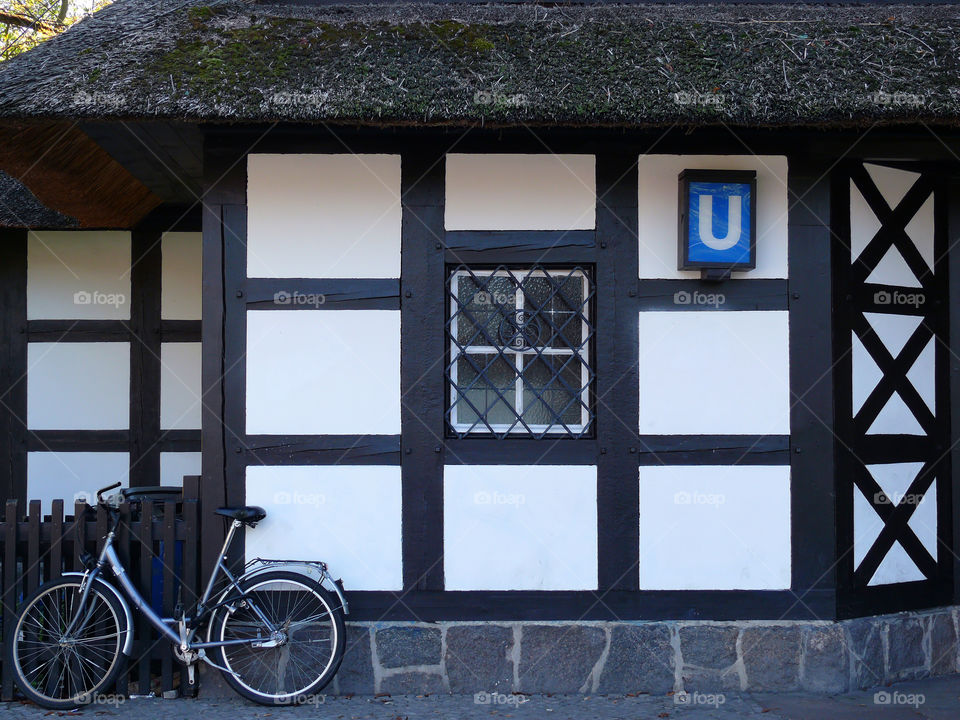 Bicycle connected to wooden fence of metro station Dahlem Dorf which entrance is constructed as a cottage. Berlin, Germany.