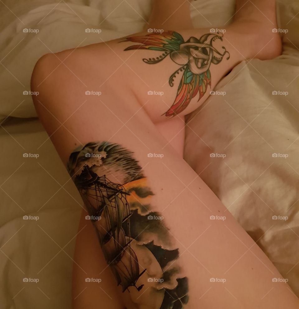 long tattooed legs having a rest in bed on satin sheets. fairy tattoo, pirate ship tattoo